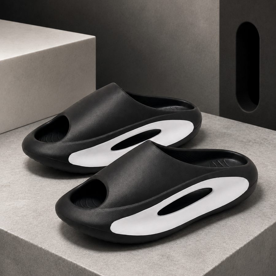 Pair of black Soren sculpted EVA slides with white side inserts on a warm white background.